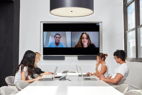 People in a meeting room, two of which are attending via google hangout