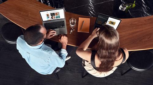 Two people working together on laptops, seen from above.