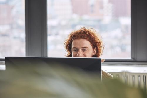 Person smiling, sitting behind a computer screen.