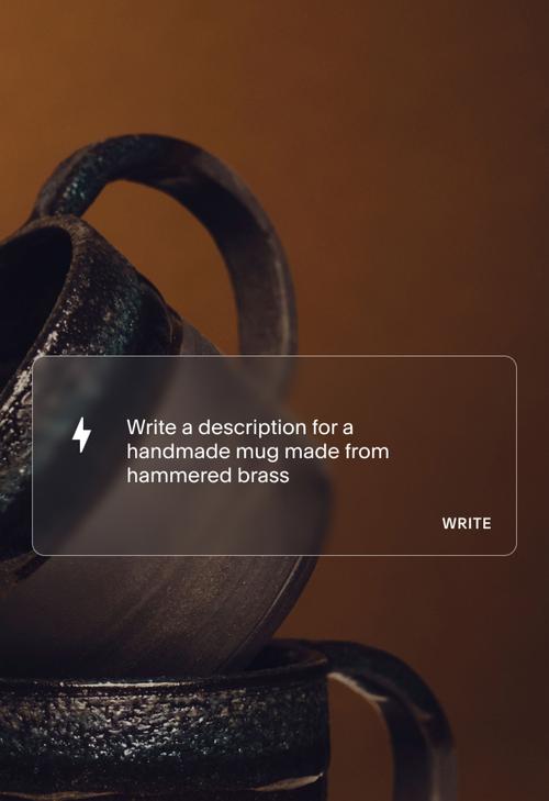 A close-up photo of a handmade mug with a dark, aged patina. A translucent interface overlay contains a writing prompt that says "Write a description for a handmade mug made from hammered brass," next to a clickable button labeled "WRITE."