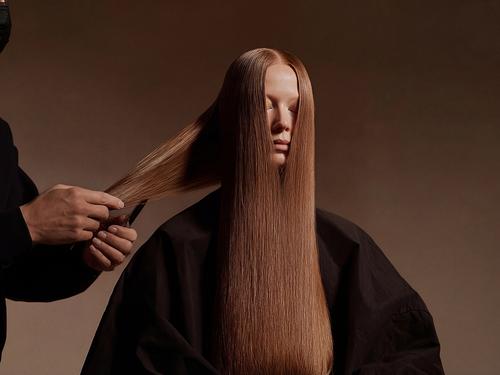 Die Hände eines Friseurs schneiden das lange, glatte, kastanienbraune Haar einer Frau, die mit geschlossenen Augen dasitzt.