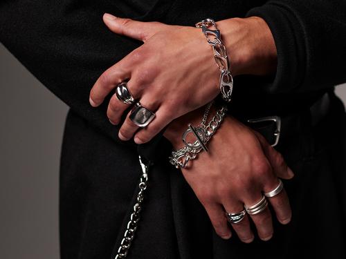A close-up of a person's hands wearing and holding various heavy silver chains, link bracelets, and thick metal rings.