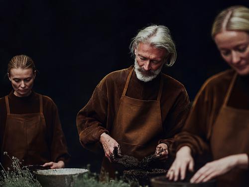 갈색 앞치마와 상의를 맞춰 입은 진지한 표정의 사람들이 환경 보호 활동을 위해 흙과 식물을 다루는 일에 집중하고 있는 모습