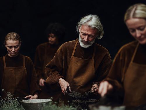 A serious-looking group of people in matching brown aprons and tops, focusing on working with soil and plants for conservation efforts.