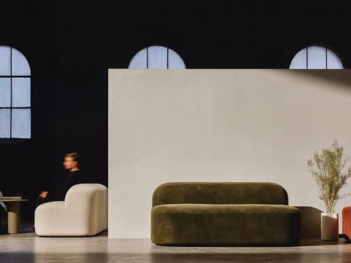 둥글고 푹신한 소파 두 개와 아치형 창문, 배경에 모션 블러 처리된 남성이 앉아 있는 현대적인 사무실 또는 라운지 공간