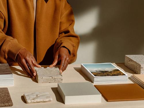 질감이 있는 돌이나 샘플 타일을 다른 재료 샘플과 가죽 스와치, 영감을 주는 사진들 사이에 놓고 있는 사람의 손