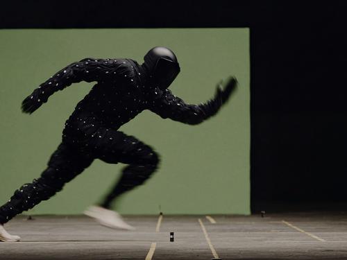 그린 스크린 배경 앞에서 헬멧을 쓰고 전체 검은색 모션 캡처 수트를 입은 채 달리고 있는 사람