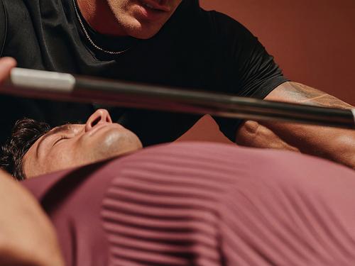 벤치프레스에 누워 바벨을 들어 올리는 사람을 트레이너 또는 코치가 돕는 클로즈업 장면